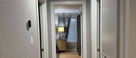 A hallway with a wooden floor, a door on the right, and a light fixture on the ceiling.