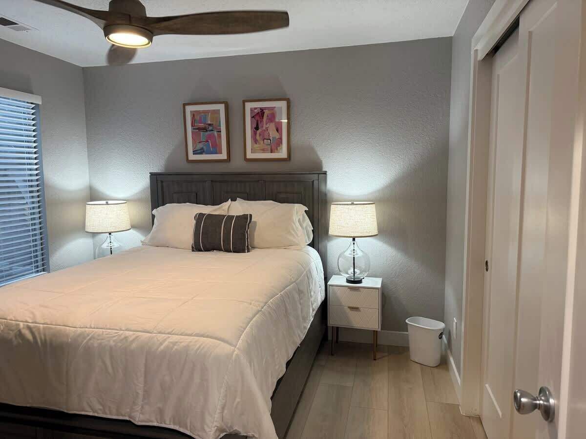 A bedroom with a bed, two bedside lamps, a ceiling fan, and two framed pictures on the wall.