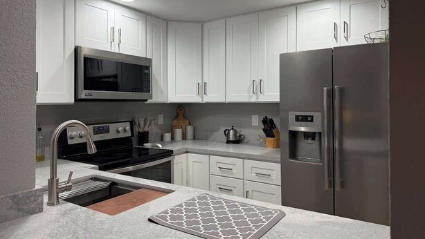 A modern kitchen with white cabinets, stainless steel appliances, a microwave, oven, sink, and a refrigerator. - Modern Blue Marina 2 bed 2 bath garage whole home (Modesto)