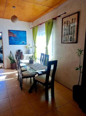A dining area with a glass table, chairs, a painting, and a framed picture on the wall.