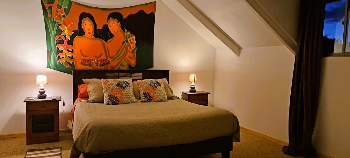 A bedroom with a bed, two bedside tables, a nightstand, a large painting, and a window with curtains.
