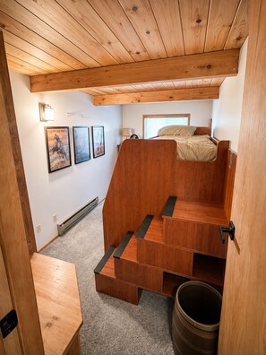 Une pièce de taille modeste, avec un lit superposé, un plafond en bois et une petite fenêtre.