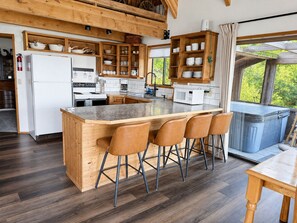 A modern kitchen with wooden cabinets, a central island with bar stools, and a view of greenery outside. - Spectacular views from cabin in Cle Elum. Hiking, fishing, ATVs, and breweries! (Cle Elum)