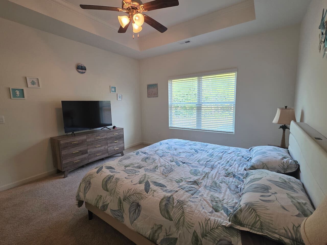 A bedroom with a bed, a dresser, a television, and a ceiling fan.