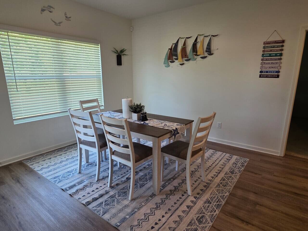 A dining area with a table and four chairs, a patterned rug, and a wall with motivational signs.
