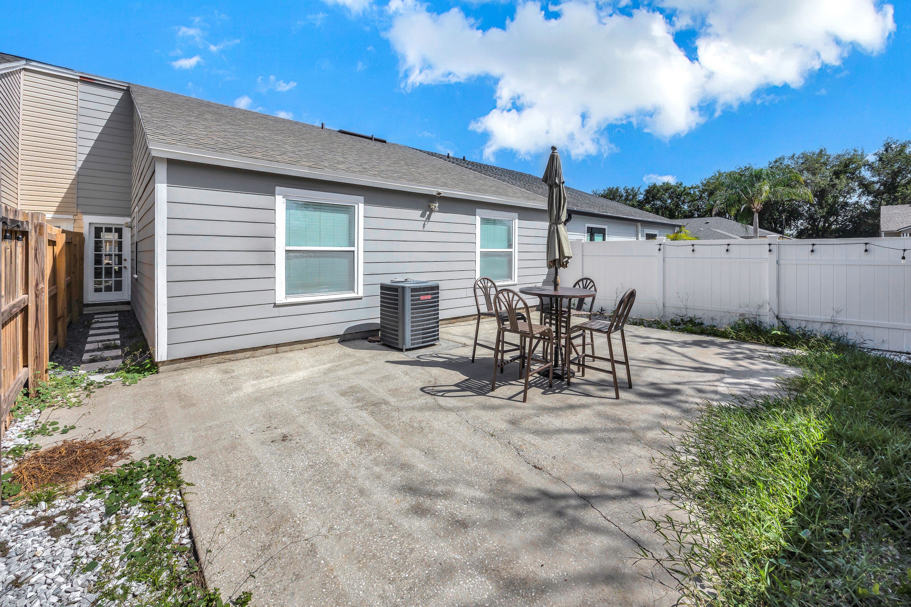 A residential backyard with a patio, a table with chairs, a trash can, and a wooden fence.