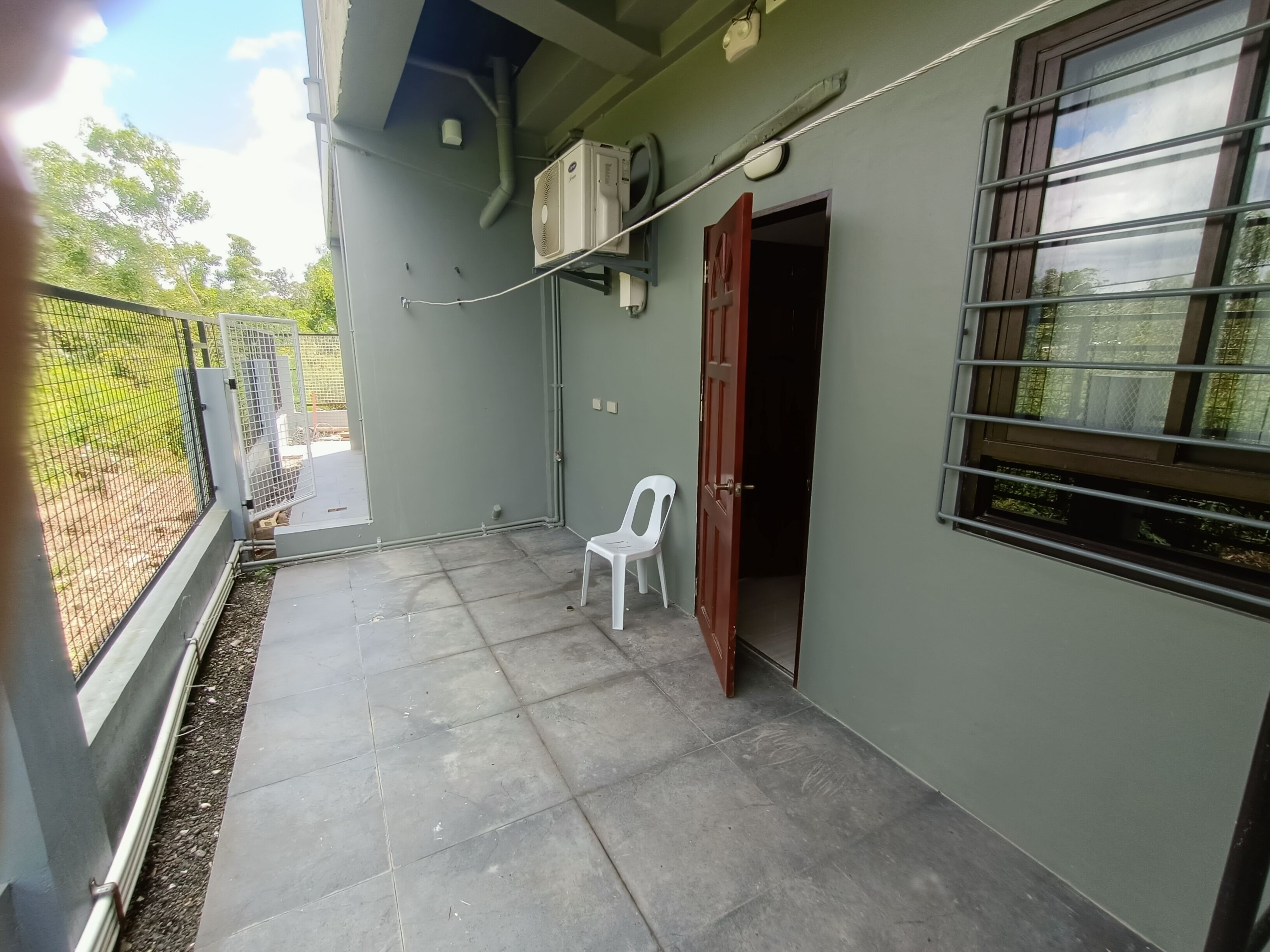 A small, enclosed outdoor area with a tiled floor, a white plastic chair, and a door leading to a dark interior.