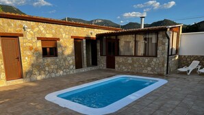 Una casa de piedra con piscina, porche cubierto y vista a la montaña.