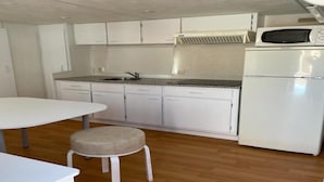 Una cocina compacta con gabinetes blancos, un microondas, un refrigerador, un lavamanos y un taburete pequeño.