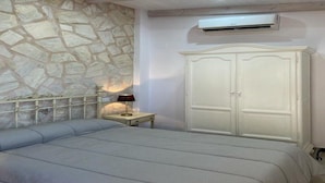 Un dormitorio con pared de piedra, una cama, una mesita de noche con lámpara y un armario.