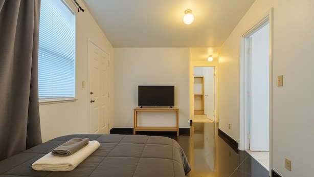 A hotel room with a bed, a TV on a stand, a door, and a hallway. - Modern Studio in the Heart of Wynwood (Miami)