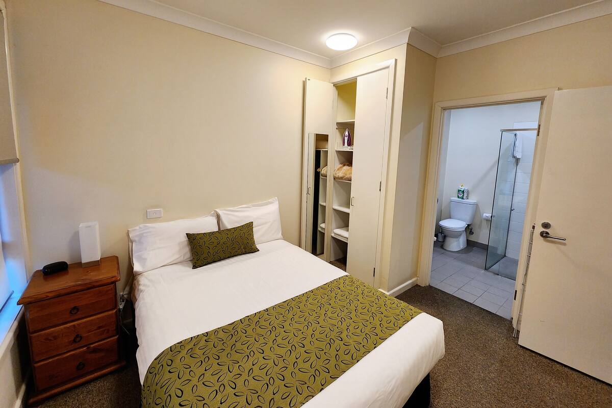 Quarto de hotel com cama, penteadeira, armário e banheiro com chuveiro.