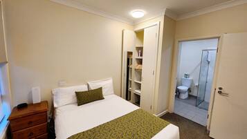 A hotel room with a bed, a dresser, a closet, and a bathroom with a shower.