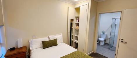A hotel room with a bed, a dresser, a closet, and a bathroom with a shower.