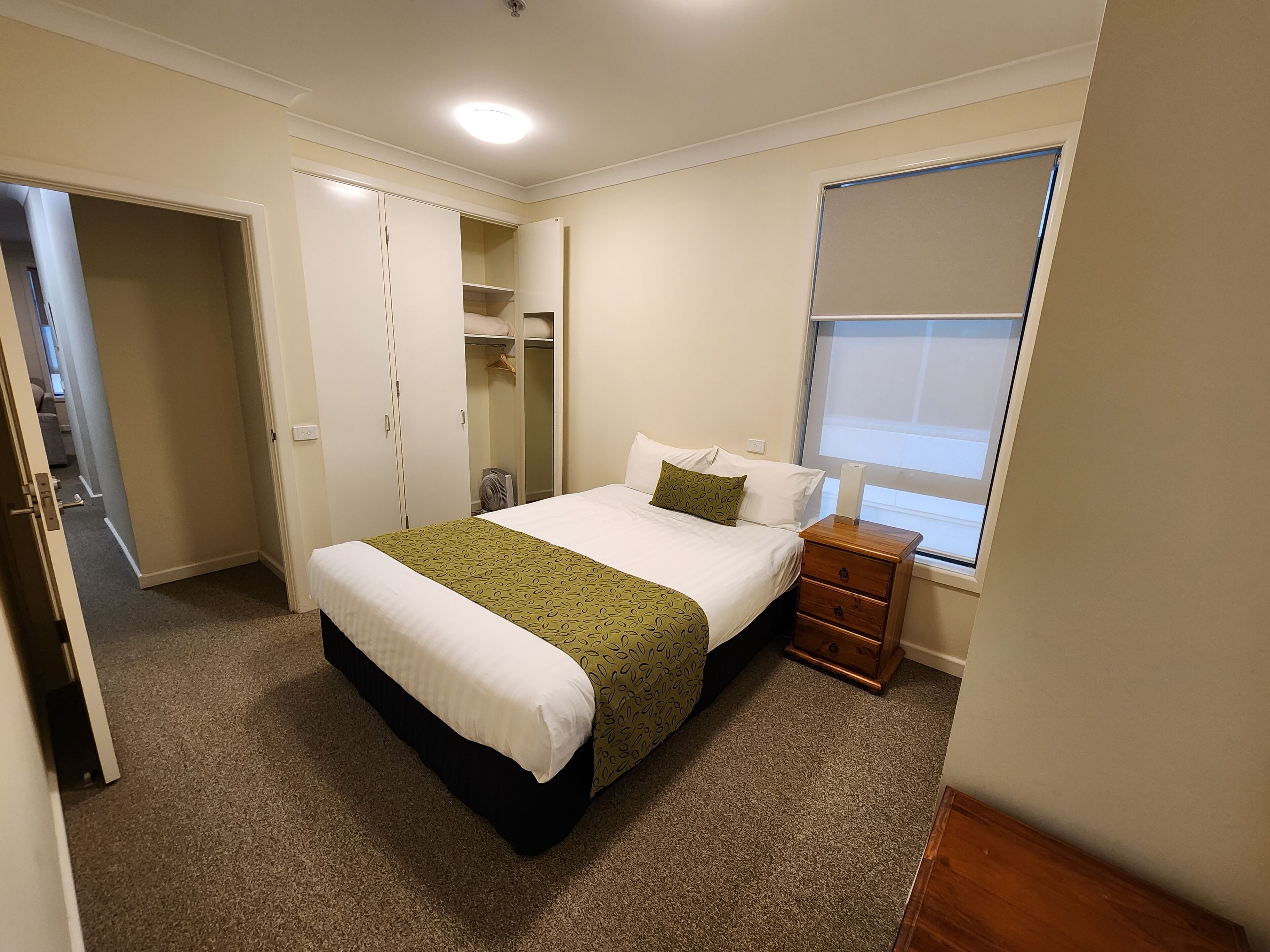 A bedroom with a bed, a nightstand, a wardrobe, and a window.