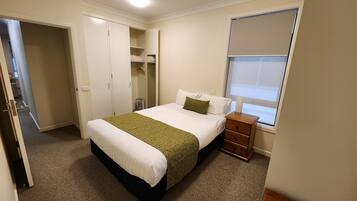 A bedroom with a bed, a nightstand, a wardrobe, and a window.