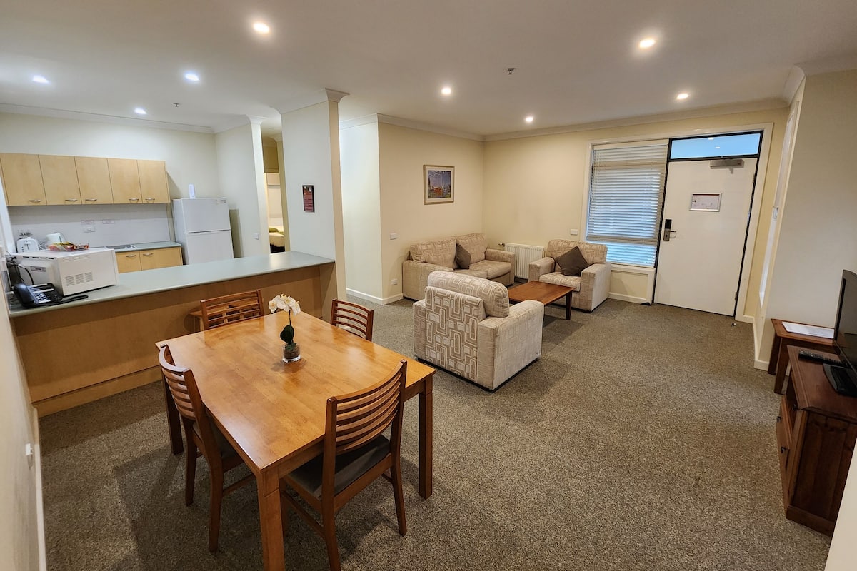 Um espaço compacto com cozinha americana, área de refeições e sala de estar com sofás e mesa de centro.