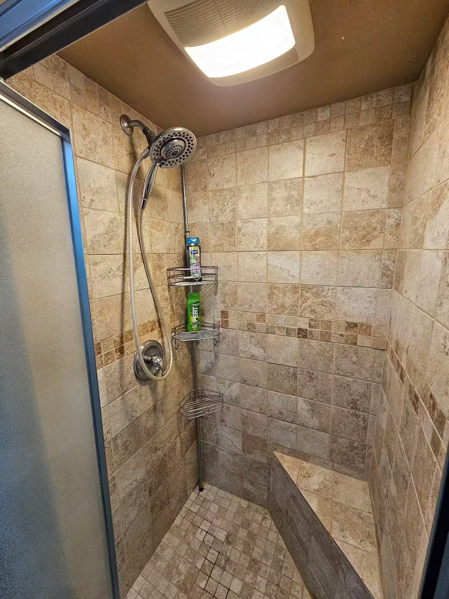 Une douche équipée d’un pommeau de douche à main, d’un robinet mural et d’une étagère pour les articles de toilette.