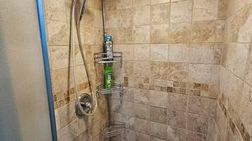 Une douche équipée d’un pommeau de douche à main, d’un robinet mural et d’une étagère pour les articles de toilette.