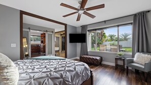 A bedroom with a large bed, a ceiling fan, a TV, and a view of the outdoors. - NEW! FOUNTAIN PALMS OASIS HEATED POOL (Fountain Hills)