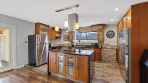 A modern kitchen with a central island, stainless steel appliances, wooden cabinets, and a stone backsplash. - NEW! FOUNTAIN PALMS OASIS HEATED POOL (Fountain Hills)