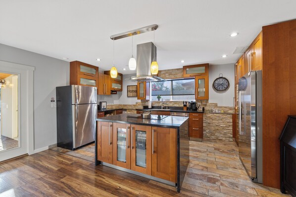 A modern kitchen with a central island, stainless steel appliances, wooden cabinets, and a stone backsplash.
