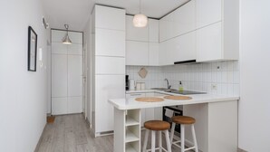 A compact kitchen with white cabinets, a white countertop, two stools, and a hanging pendant light. - Park Krakowski Comfy Studio (Kraków)