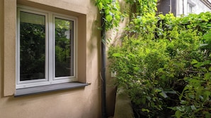 A window with a white frame and a small ledge below it, surrounded by dense green foliage. - Park Krakowski Comfy Studio (Kraków)