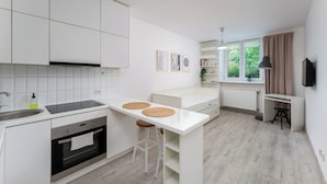 A modern kitchen with white cabinetry, a built-in oven, a sink, and a dining area with stools. - Park Krakowski Comfy Studio (Kraków)