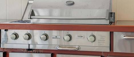 A stainless steel grill with a control panel and multiple storage drawers.