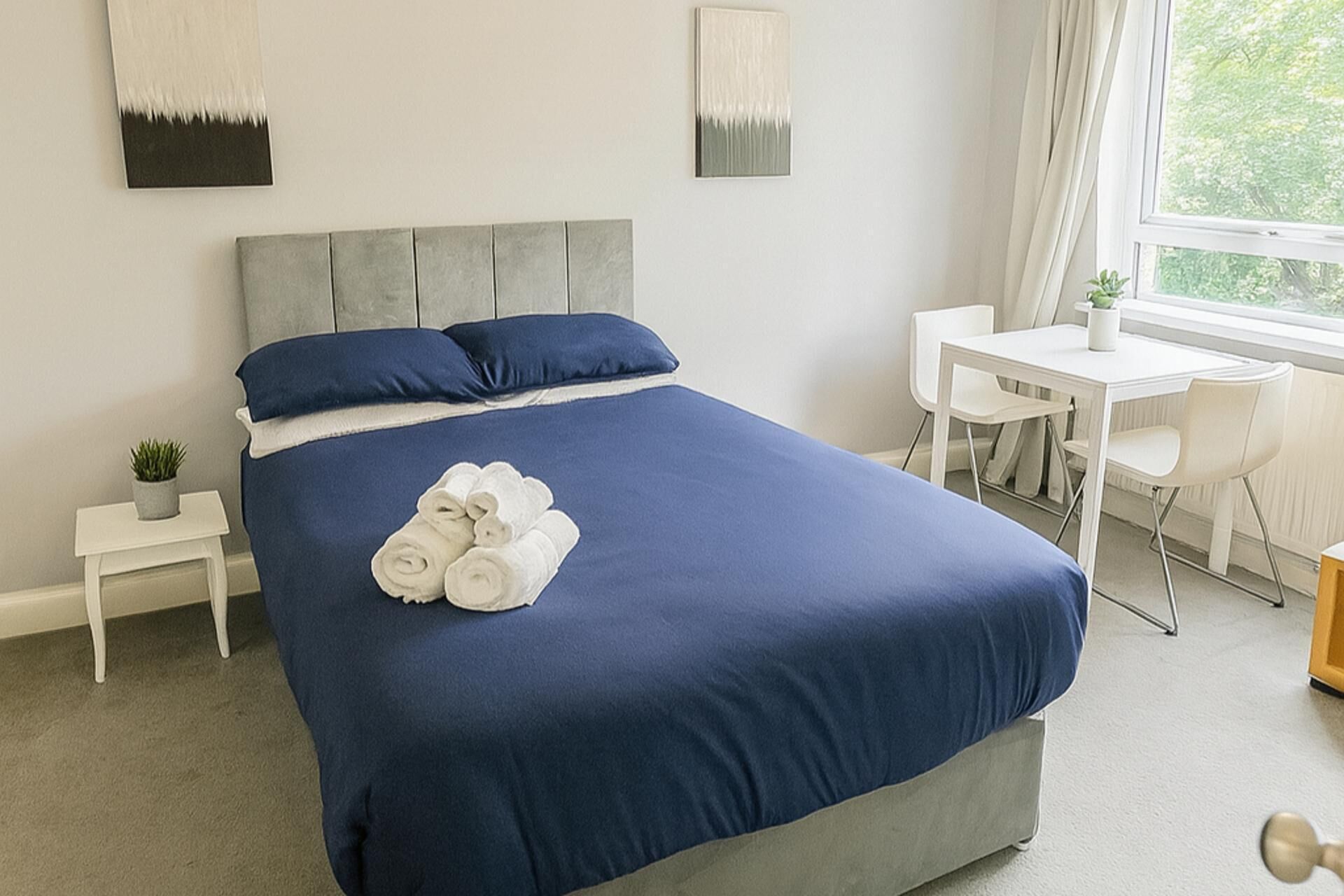 Une chambre bien rangée, avec un grand lit, une petite table et une chaise.