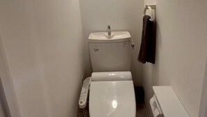 Un baño pequeño y blanco con inodoro, lavamanos y perchero para toallas.