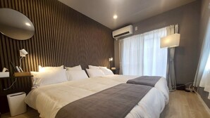 Una habitación de hotel moderna con una cama grande, una mesita de noche, una lámpara y un equipo de aire acondicionado.