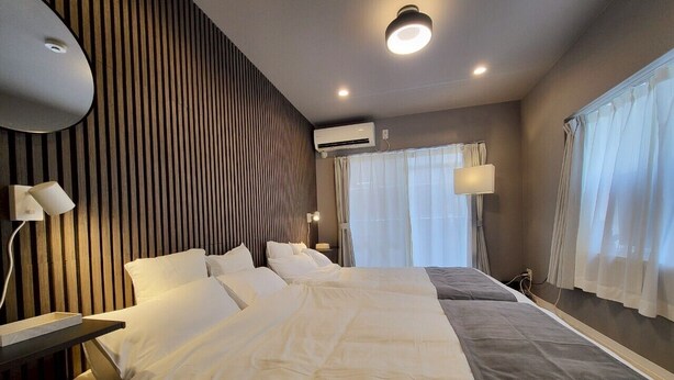 Habitación de hotel con una cama grande, una mesita de noche, una lámpara, equipo de aire acondicionado y una ventana con cortinas.