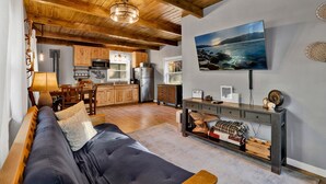 Una sala de estar acogedora con un sofá, un comedor con mesa y sillas, una cocina con armarios de madera y un televisor grande montado en la pared.