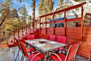 A dining area with a table and chairs, a staircase, and a view of trees and a building in the background.