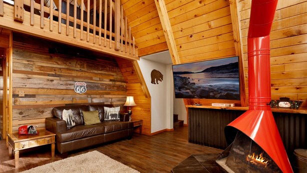 Interior acogedor de una cabaña con detalles de madera, un sofá de cuero, una chimenea y un televisor en la pared.