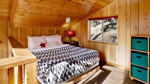 Un dormitorio de cabaña de madera con cama, mesita de noche, ventana y almacenamiento empotrado.