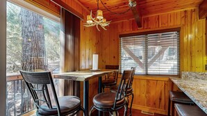 Un interior de madera con un comedor que incluye una mesa, sillas, un banco y un amplio ventanal con persianas.