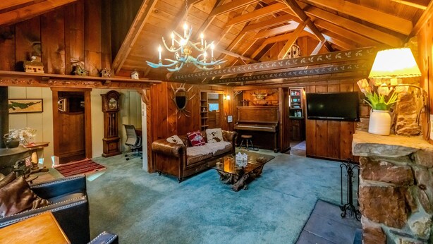Un interior rústico con vigas de madera, una araña, un piano y una chimenea.