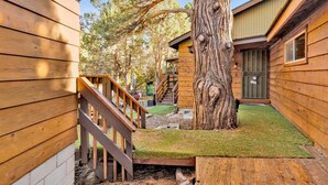 A wooden cabin with a staircase leading to a deck, surrounded by trees.