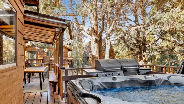 A wooden deck with a hot tub, barbecue grill, and outdoor seating area.