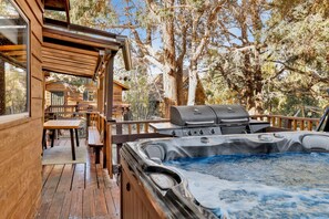 A wooden deck with a hot tub, barbecue grill, and outdoor seating area.