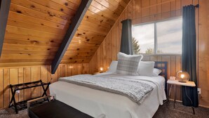 Una habitación con paneles de madera, una cama, un banco y una ventana con cortinas.