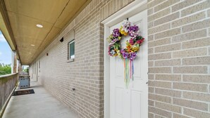 A covered porch with a brick wall, a white door with a floral wreath, and a small window.