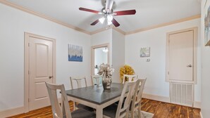 A dining room with a dark wooden table, white chairs, a ceiling fan, and a wooden floor.