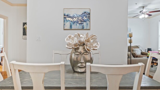A dining area with a table set for two, a decorative vase, and a painting on the wall.