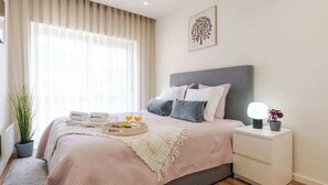 Een moderne slaapkamer met een bed, nachtkastje en een raam met gordijnen.
