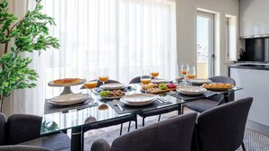 Een eethoek met een glazen tafel gedekt voor het ontbijt, inclusief borden, glazen en diverse soorten eten.