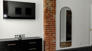 Un dormitorio moderno con una pared de ladrillo decorativa, un televisor de pantalla plana, un espejo grande y un aparador negro.